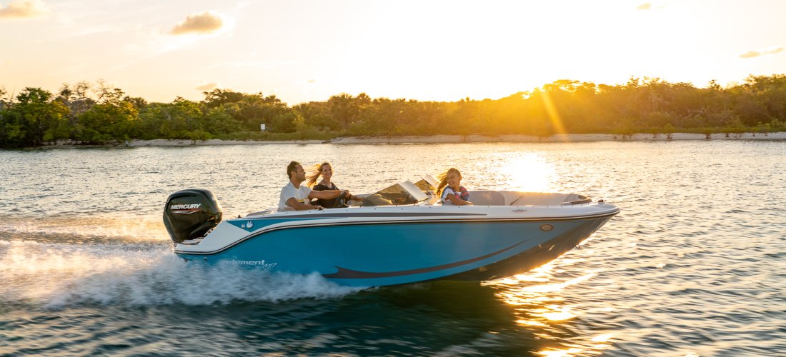 En familie sejler i deres Bayliner M17 i solnedgang. Båden ses her med en Mercury påhængsmotor.
